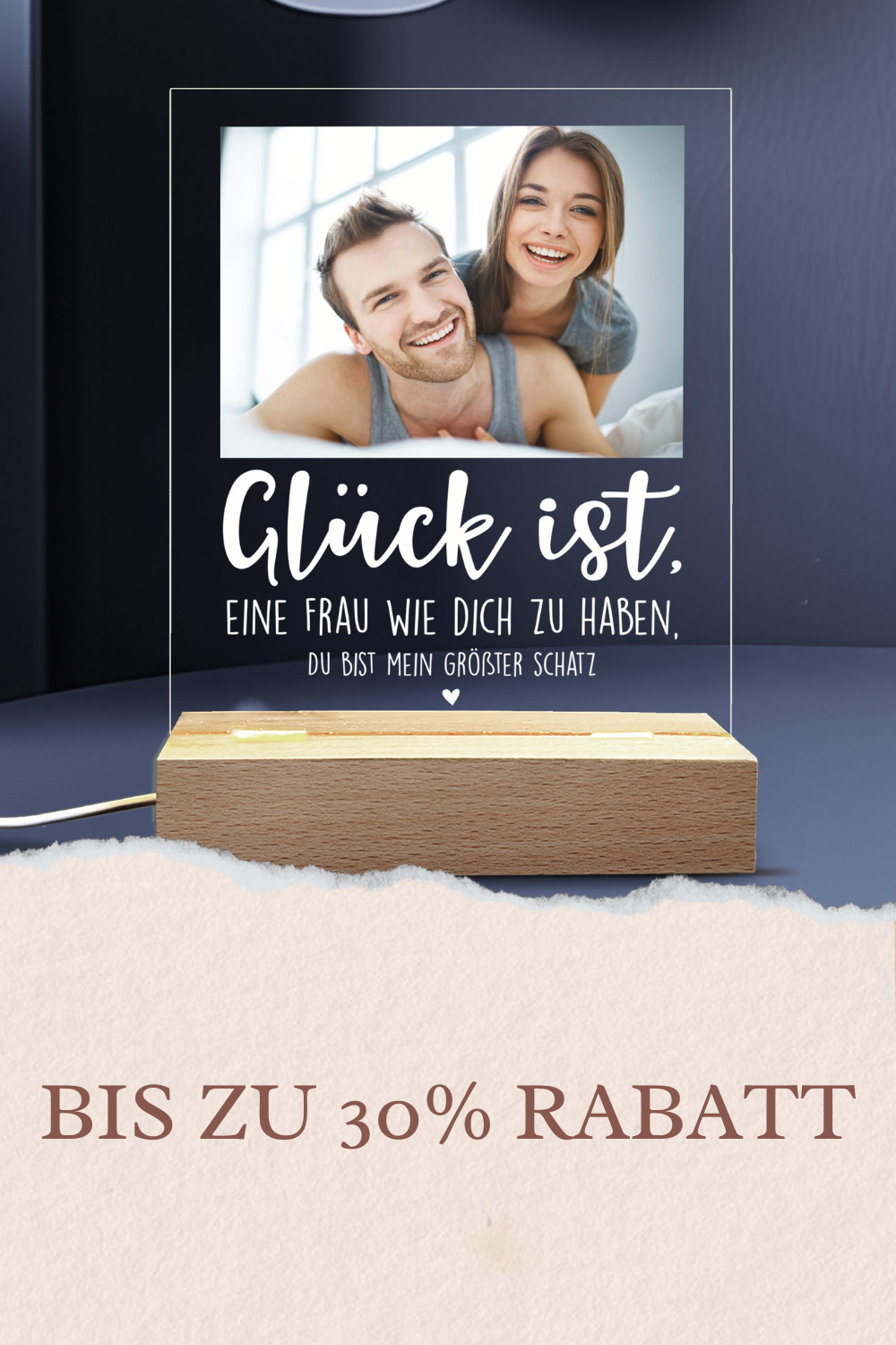 Personalisierte LED-Tischlampe in Herzform mit Foto eines Paares beim Sonnenuntergang und goldener Gravur ‚Ewig Dein‘, platziert auf einem schlichten Holztisch neben einer Geschenkbox und einem Glas Sekt. Warmes Licht erzeugt eine gemütliche Atmosphäre